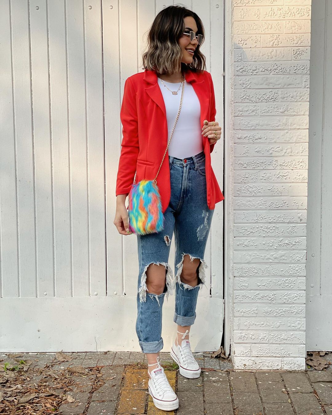 Blazer feminino vermelho despojado com camiseta branca, jeans rasgado e tênis All Star branca de cano baixo